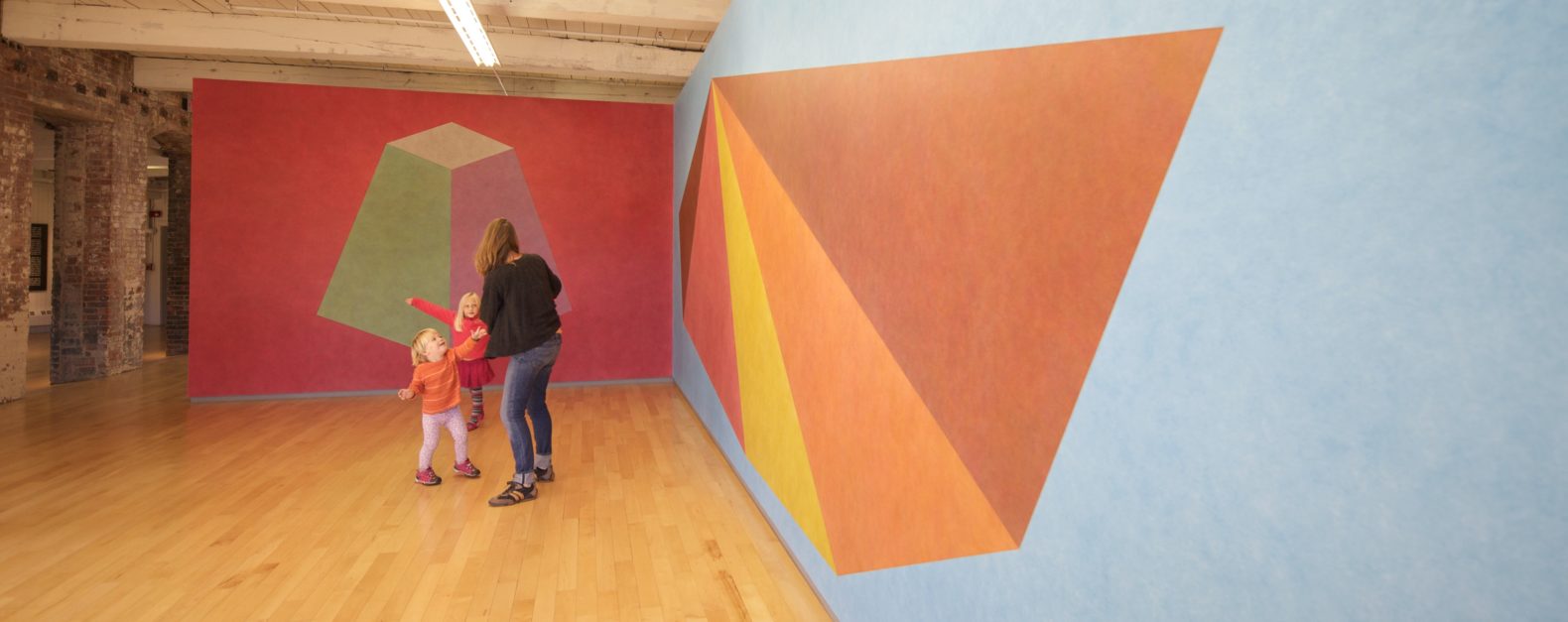 Woman in black sweater facing away from the camera and toward two children, one pointing, in Sol LeWitt