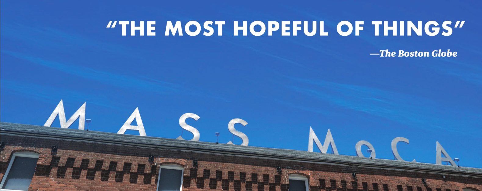 Angled up view of brick building with MASS MoCA sign and blue sky above, with text overlaid reading "The most hopeful of things"