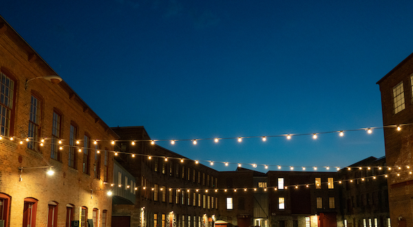 String lights between brick mill buildings during dusk