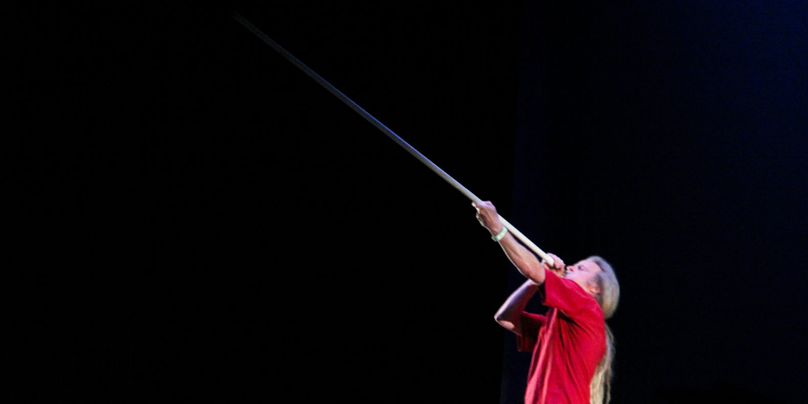 Man in red shirt blowing into long horn on stage