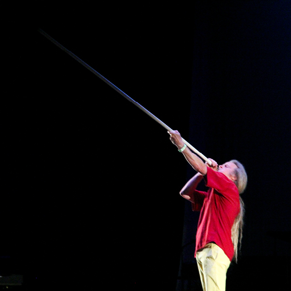 Man in red shirt blowing into long horn on stage