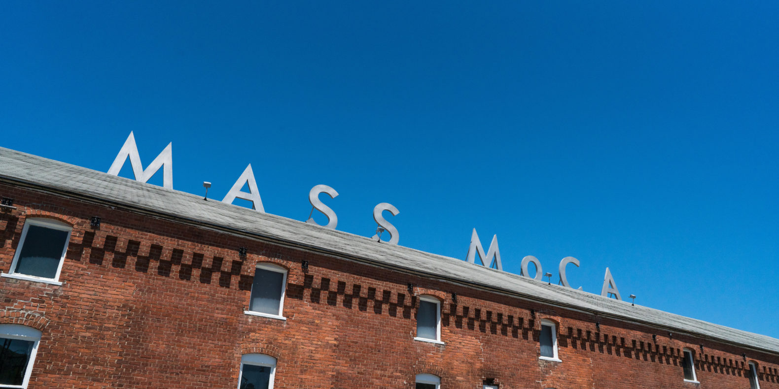 Angled up view of brick building with MASS MoCA sign and blue sky above