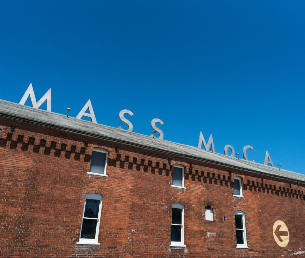 Angled up view of brick building with MASS MoCA sign and blue sky above