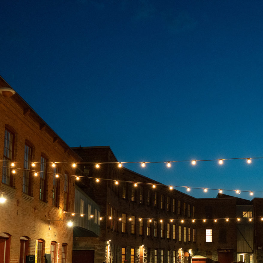 String lights between brick mill buildings during dusk