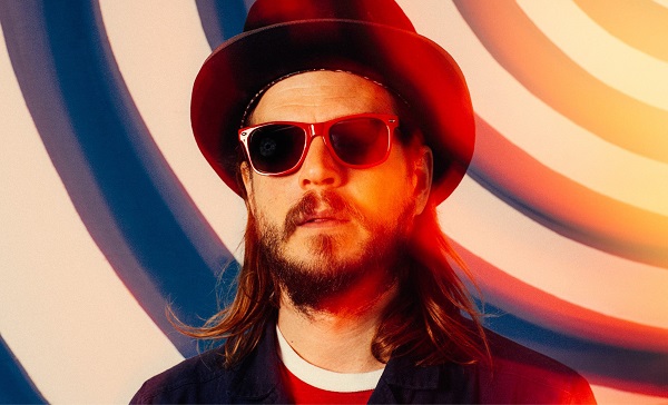 Piano player Marco Benevento in a top hat and sunglasses in front of a wall with curved blue and white stripes