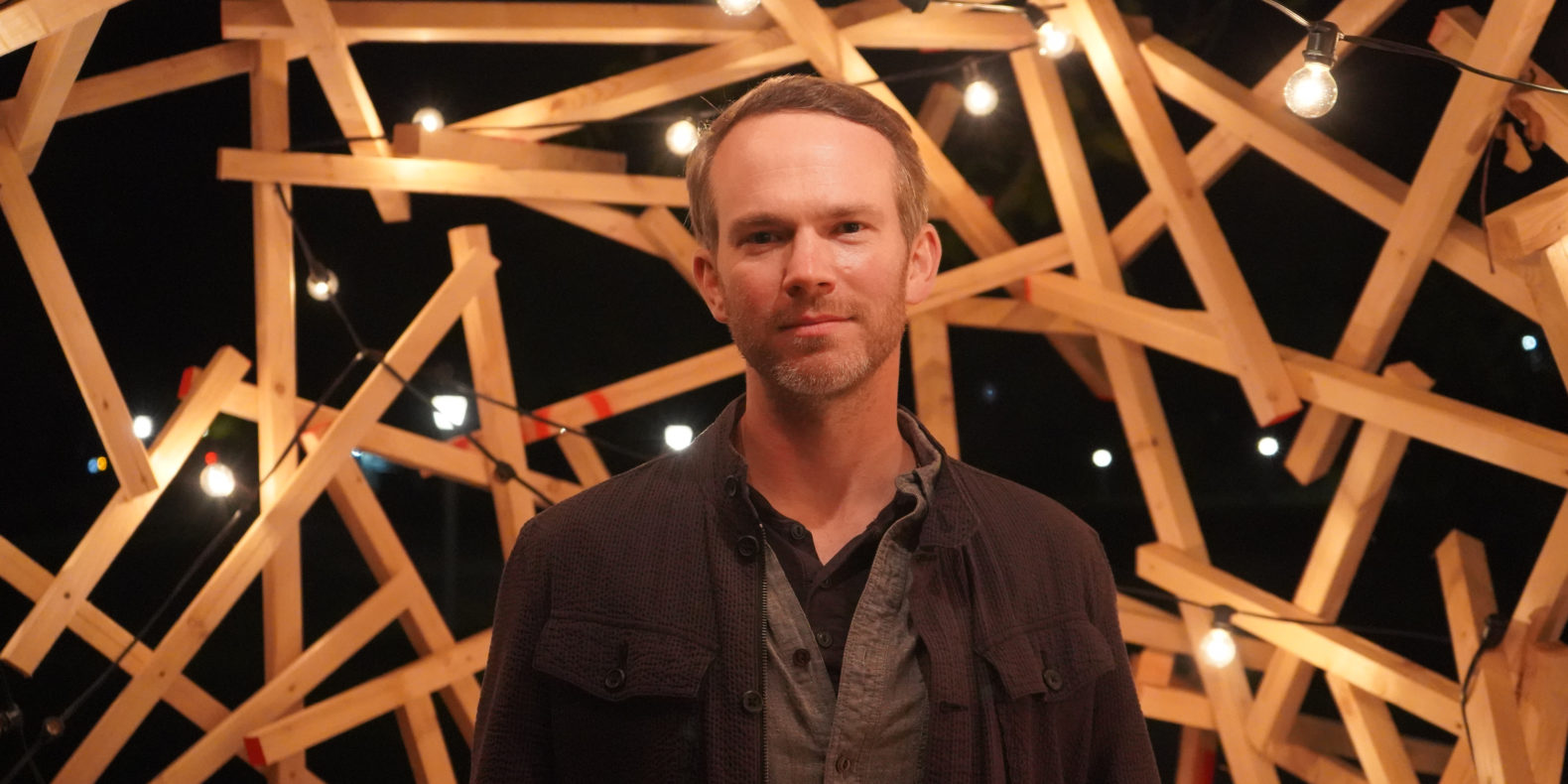 Musician Andy Wrba in front of a wooden sculpture with hanging lights