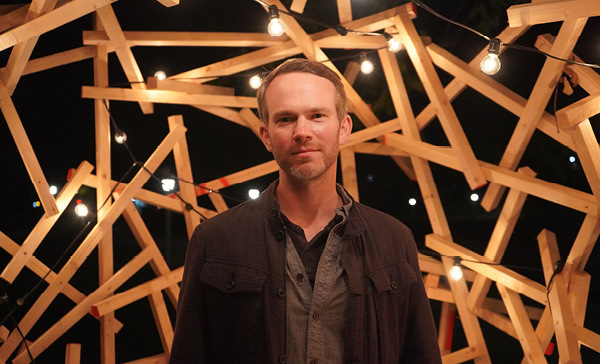 Musician Andy Wrba in front of a wooden sculpture with hanging lights