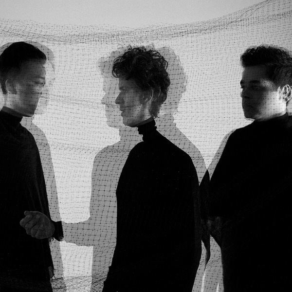 Auditory After Dark: Son Lux, blurred image of three band members dressed in black with black netting behind them
