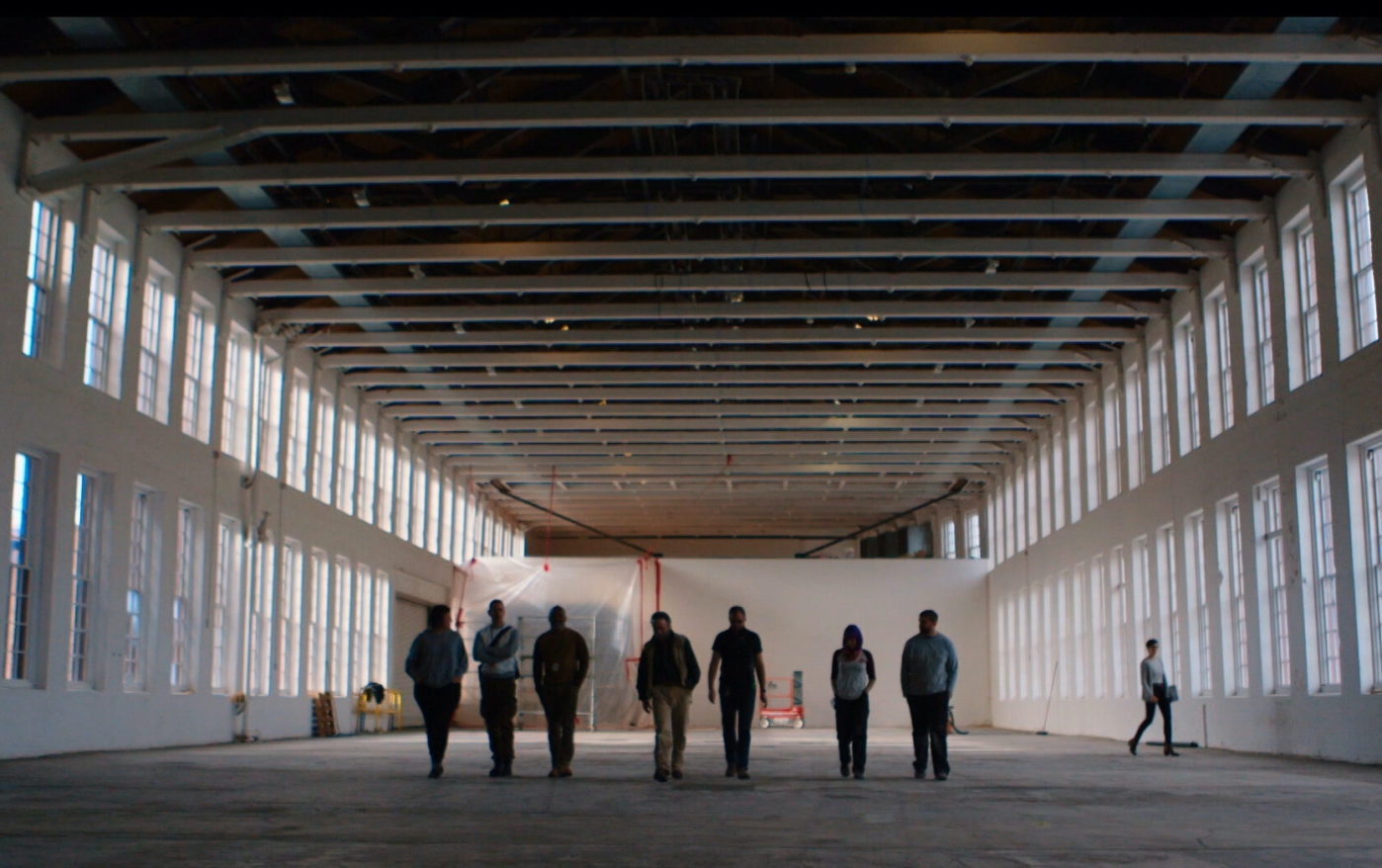 Still from film Museum Town, people walking through an empty Building 5