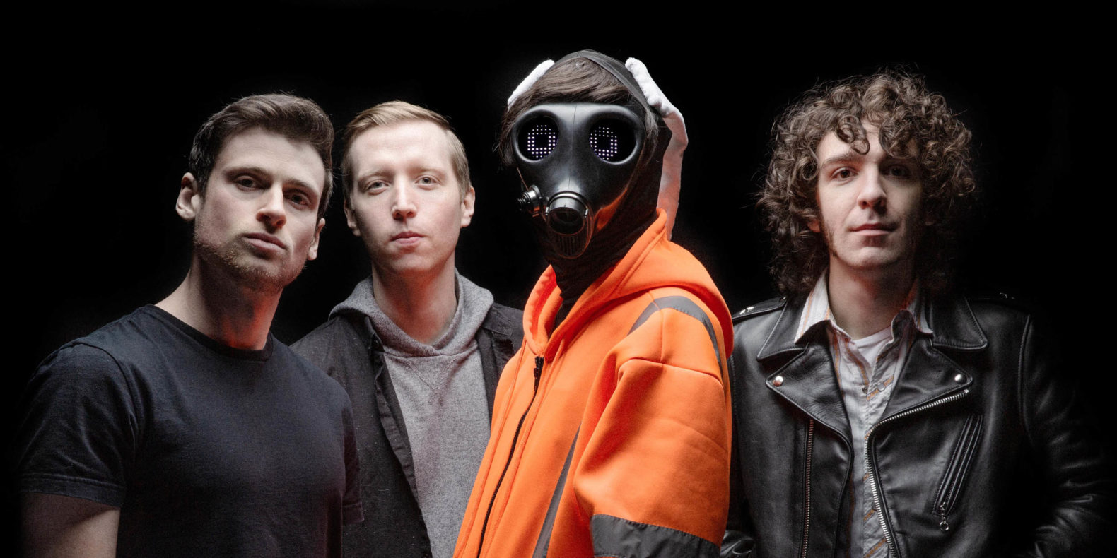 Car Seat Headrest feature image, four band members against black background, Will Toledo in orange sweatshirt with black gas mask on