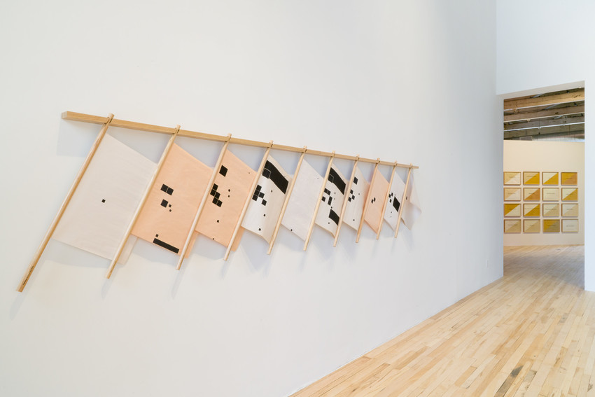 Installation view of Aslı Çavuşoğlu: With Just the Push of a Voice in the exhibition Kissing through a Curtain (MASS MoCA, 2020). Works visible (left-right): Aslı Çavuşoğlu, The Mourning Herald, 2020 Screen print on newsprint, wood rack Courtesy of the artist Aslı Çavuşoğlu, Not Equal To [USA], 2019 14 drawings with squid ink on restored paper Courtesy of the artist